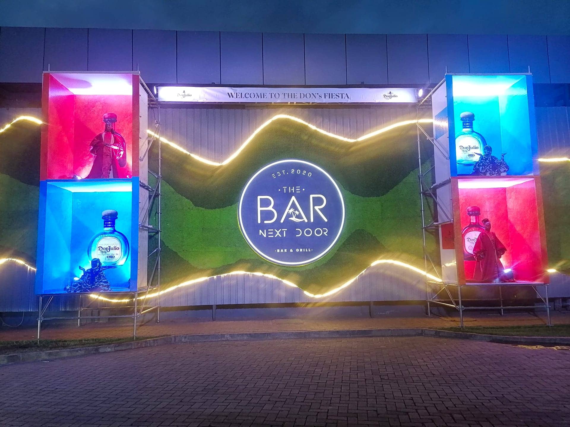 An illuminated outdoor entrance wall with backlit product-display towers flanking a central signage roundel at night