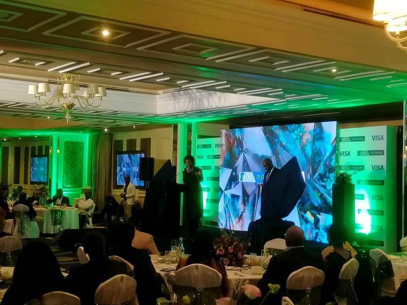 Cover of the KCB Platinum Launch album: a host on stage at a podium beside a large LED wall with green uplighting and a seated audience