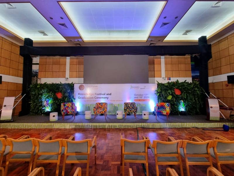 Cover of the OnePlanet Fellowship album: a conference stage with green foliage walls and colourful African-print armchairs