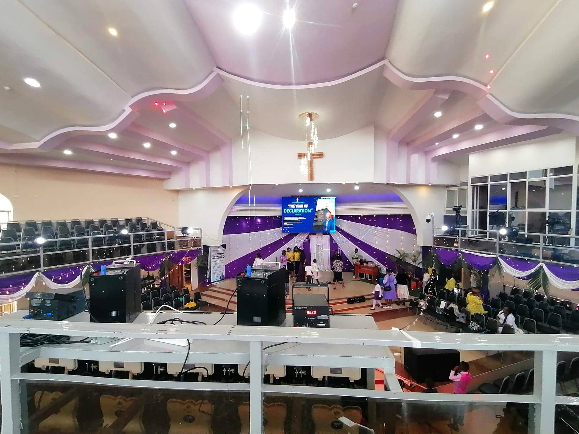 A purple-draped auditorium with stage uplighting, a wooden cross and a large 'Year of Declaration' LED screen